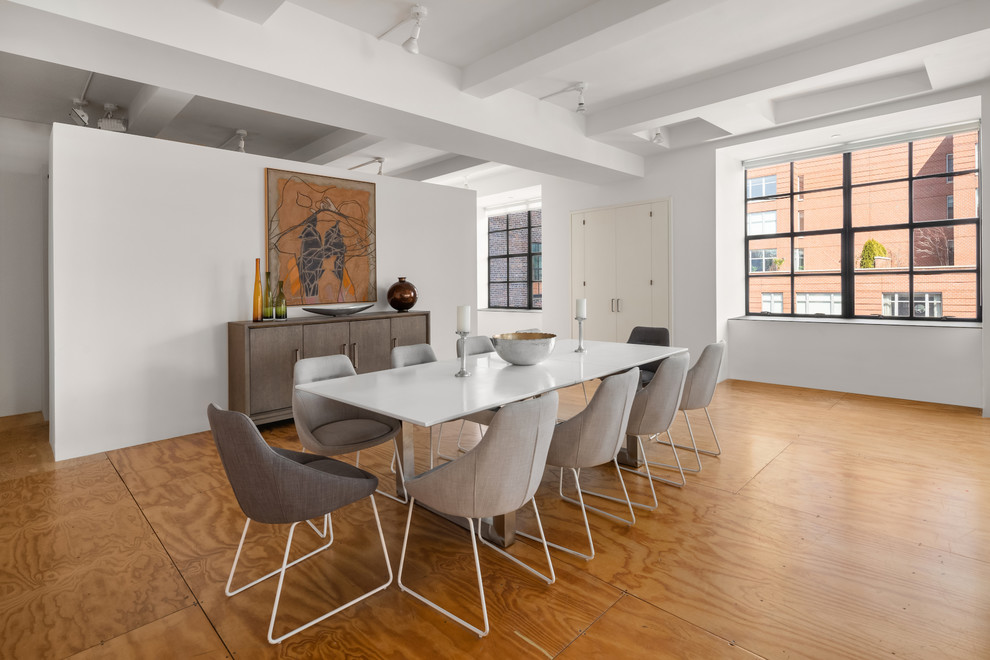 Cette image montre une salle à manger design avec un mur blanc, un sol en contreplaqué et un sol marron.