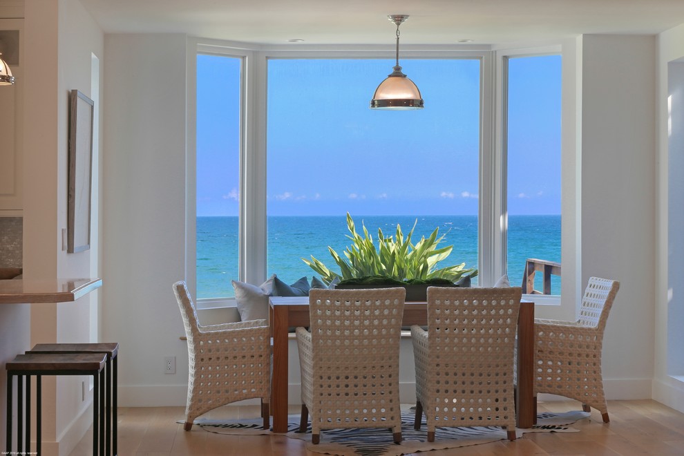 Immagine di una sala da pranzo aperta verso il soggiorno costiera con pareti bianche, pavimento in legno massello medio e pavimento marrone