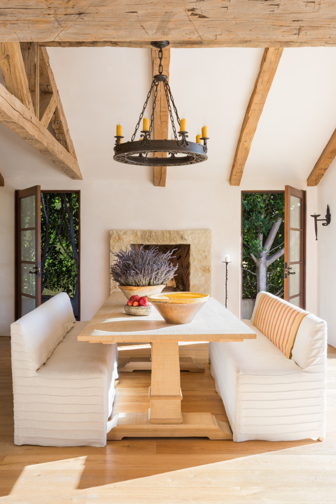 Exemple d'une salle à manger méditerranéenne de taille moyenne avec un mur beige, parquet clair, une cheminée standard, un manteau de cheminée en pierre de parement, un sol beige et poutres apparentes.