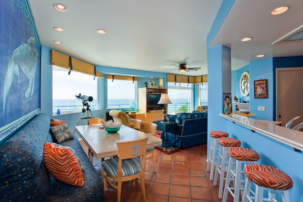 Cette image montre une petite salle à manger ouverte sur le salon ethnique avec un mur bleu et tomettes au sol.
