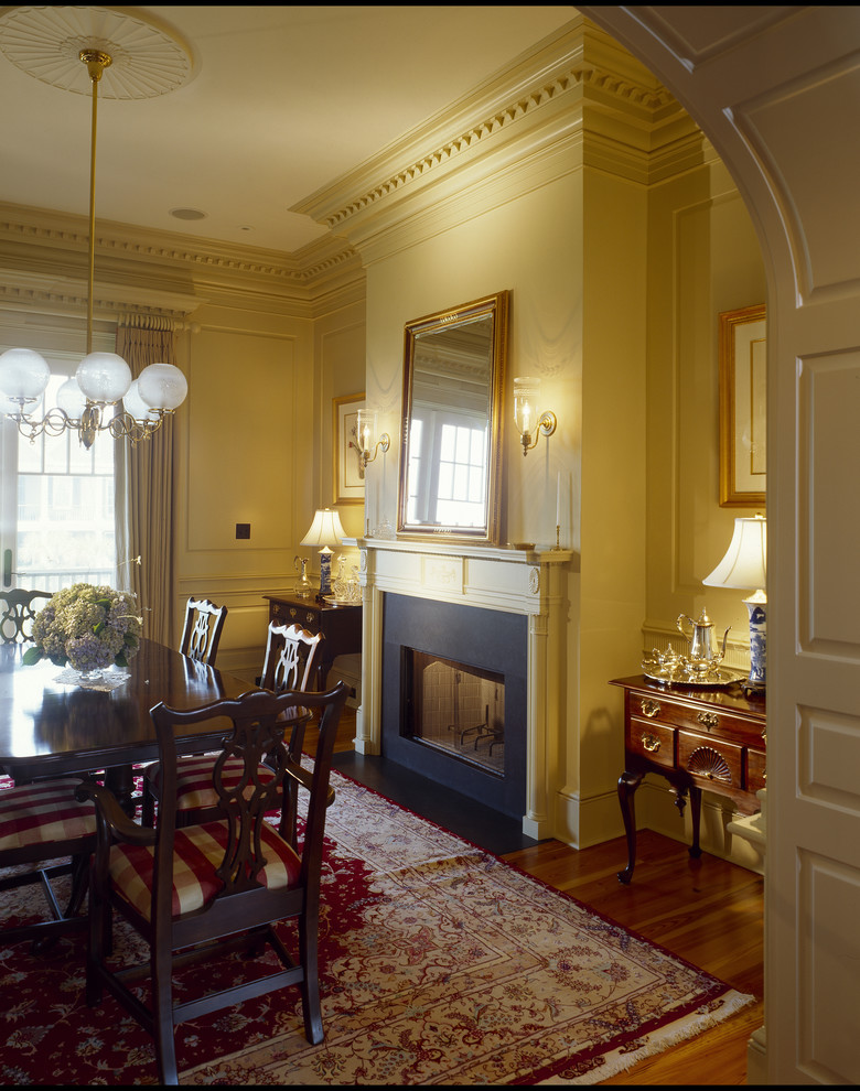 Geschlossenes, Mittelgroßes Maritimes Esszimmer mit gelber Wandfarbe, braunem Holzboden, Kamin und Kaminumrandung aus Stein in Charleston