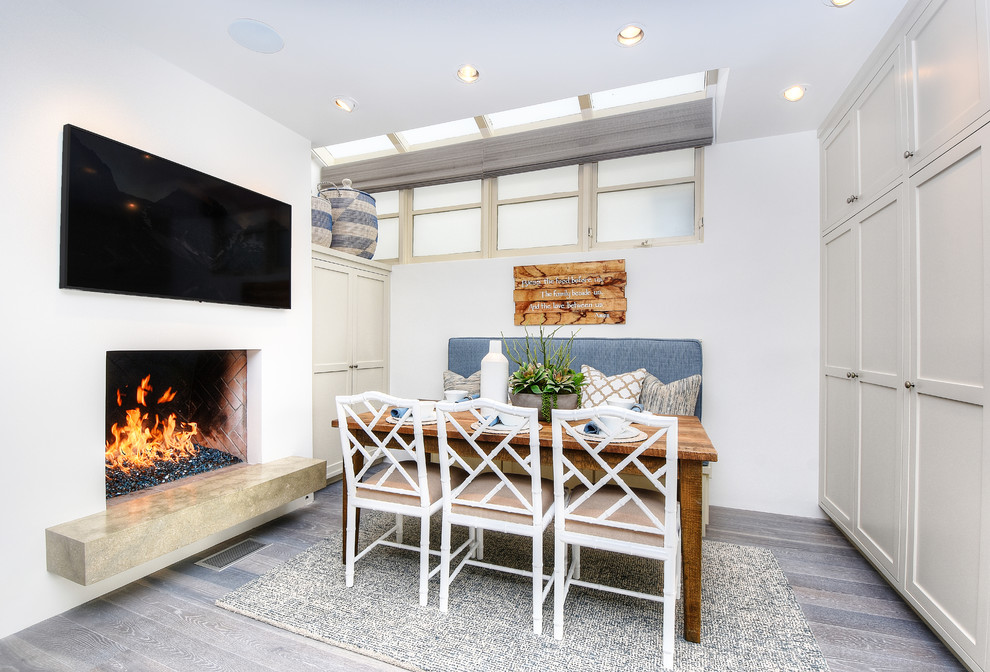 Inspiration for a small beach style open plan dining room in Orange County with white walls, a standard fireplace, grey floors and light hardwood flooring.