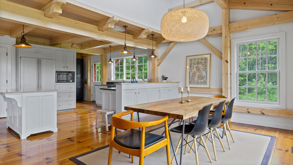 Cette photo montre une salle à manger ouverte sur le salon nature de taille moyenne avec un mur blanc, un sol en bois brun et poutres apparentes.