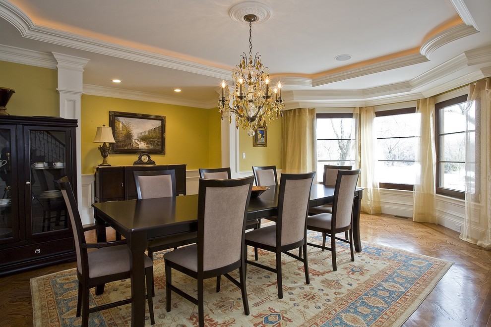 Стильный дизайн: столовая в классическом стиле с желтыми стенами и паркетным полом среднего тона - последний тренд