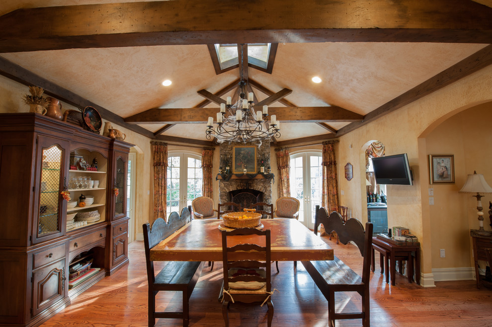 Réalisation d'une salle à manger ouverte sur la cuisine chalet de taille moyenne avec un mur beige, un sol en bois brun, une cheminée standard et un manteau de cheminée en pierre.