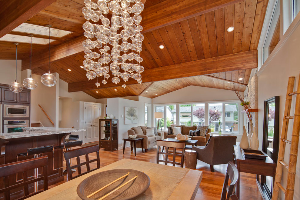 Cette image montre une salle à manger ouverte sur le salon traditionnelle de taille moyenne avec un mur beige, un sol en bois brun, une cheminée standard, un manteau de cheminée en pierre et éclairage.