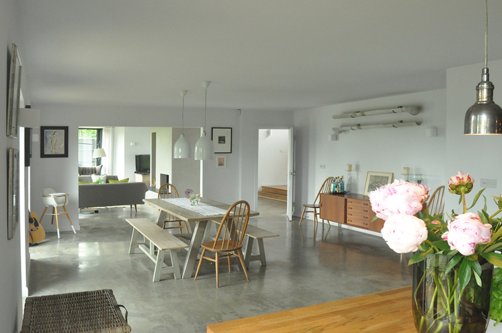 На фото: гостиная-столовая среднего размера в современном стиле с белыми стенами, бетонным полом, двусторонним камином и фасадом камина из штукатурки