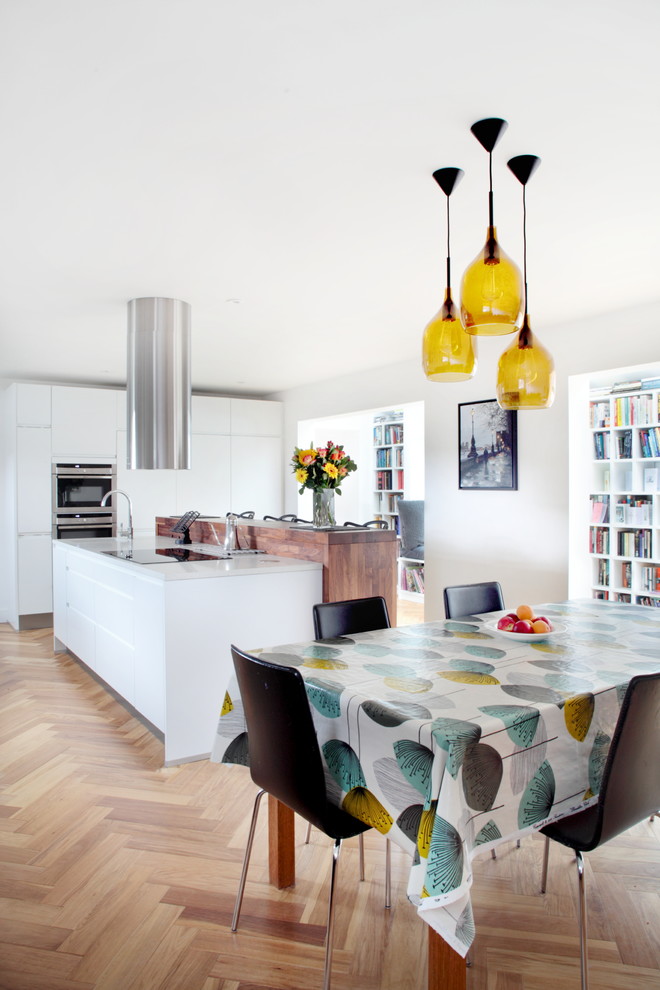 Cette image montre une grande salle à manger ouverte sur la cuisine design avec un sol en bois brun et un mur blanc.