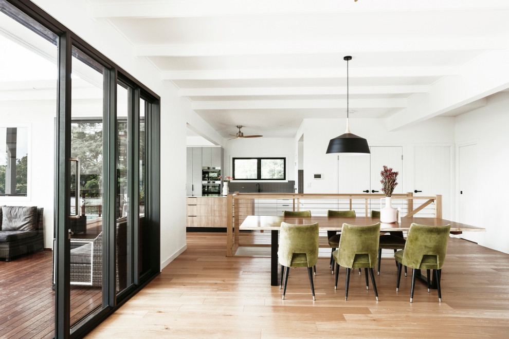 Foto di una grande sala da pranzo aperta verso la cucina moderna con pareti bianche e pavimento in legno massello medio