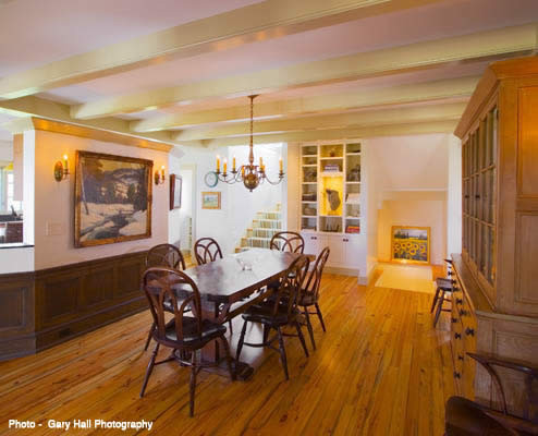 Réalisation d'une grande salle à manger tradition fermée avec un mur blanc, un sol en bois brun, une cheminée standard et un manteau de cheminée en pierre.
