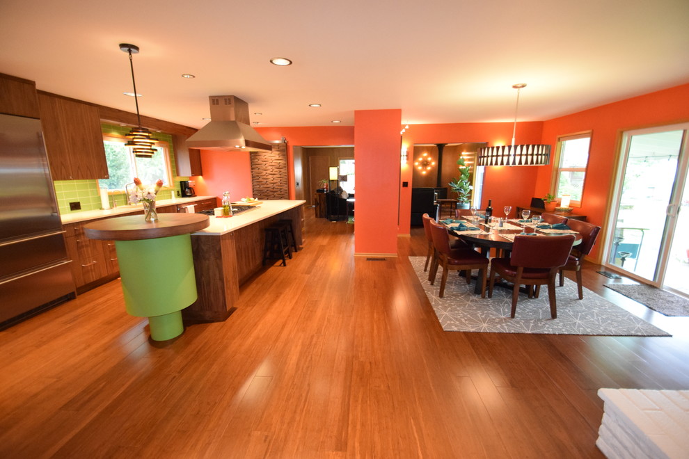Ispirazione per una grande sala da pranzo aperta verso la cucina moderna con pareti arancioni, pavimento in bambù, camino ad angolo, cornice del camino in mattoni e pavimento marrone