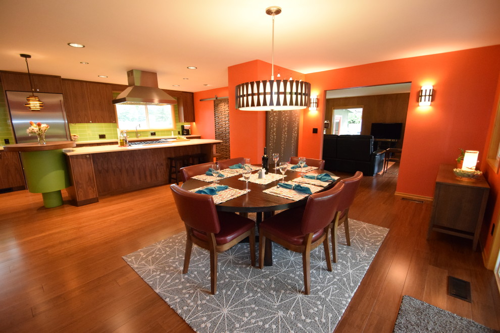 Esempio di una grande sala da pranzo aperta verso la cucina moderna con pareti arancioni, pavimento in bambù, camino ad angolo, cornice del camino in mattoni e pavimento marrone
