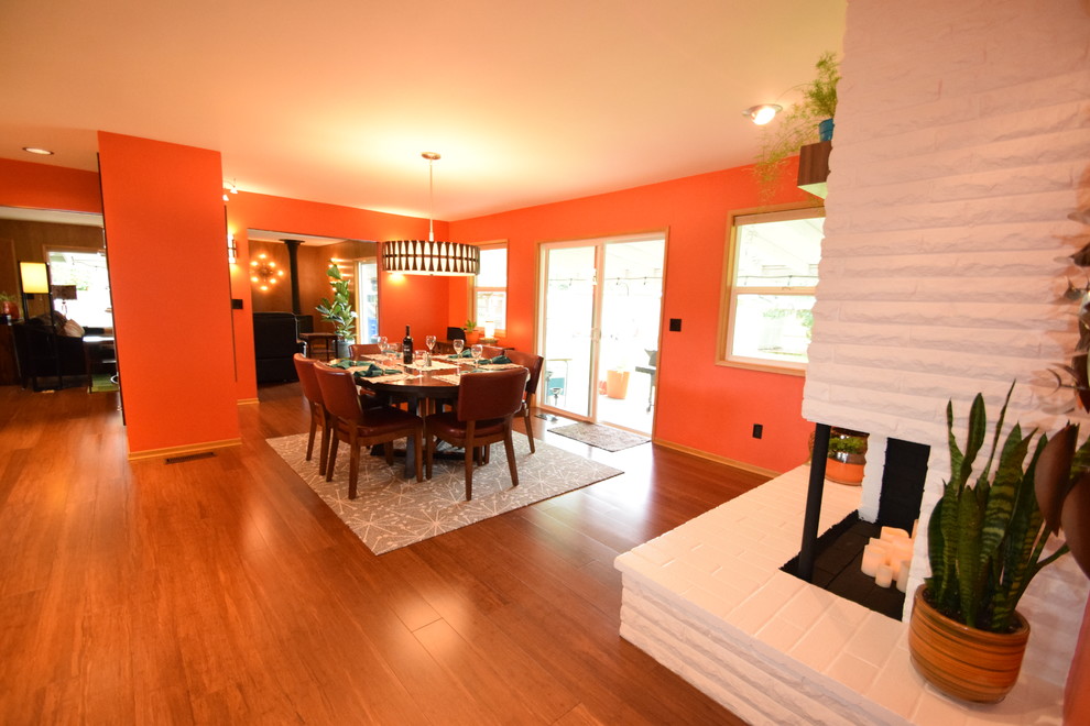 На фото: большая кухня-столовая в стиле ретро с оранжевыми стенами, полом из бамбука, угловым камином, фасадом камина из кирпича и коричневым полом с