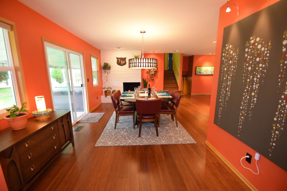50 tals inredning av ett stort kök med matplats, med orange väggar, bambugolv, en öppen hörnspis, en spiselkrans i tegelsten och brunt golv