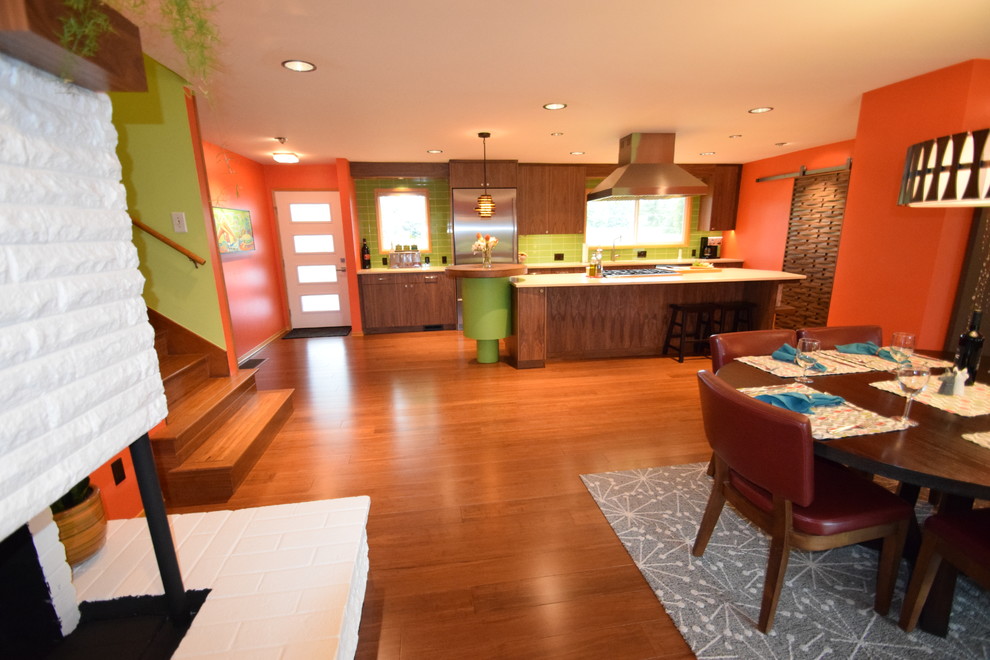 Cette image montre une grande salle à manger ouverte sur la cuisine vintage avec un mur orange, parquet en bambou, une cheminée d'angle, un manteau de cheminée en brique et un sol marron.
