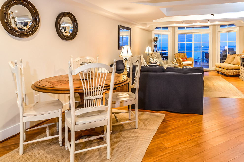 Cette image montre une grande salle à manger ouverte sur le salon marine avec un mur blanc et un sol en bois brun.