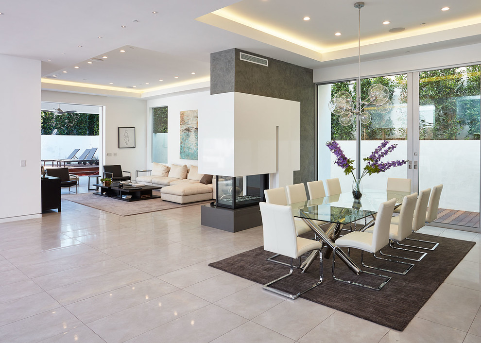 Immagine di una sala da pranzo aperta verso il soggiorno minimal con pareti bianche, camino bifacciale e pavimento grigio