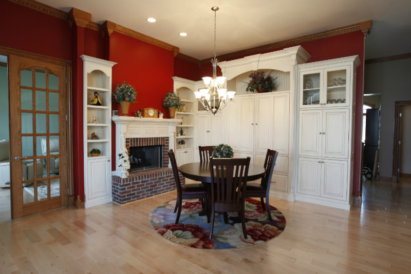 Modelo de comedor de cocina clásico pequeño con paredes rojas, suelo de madera clara, todas las chimeneas y marco de chimenea de ladrillo