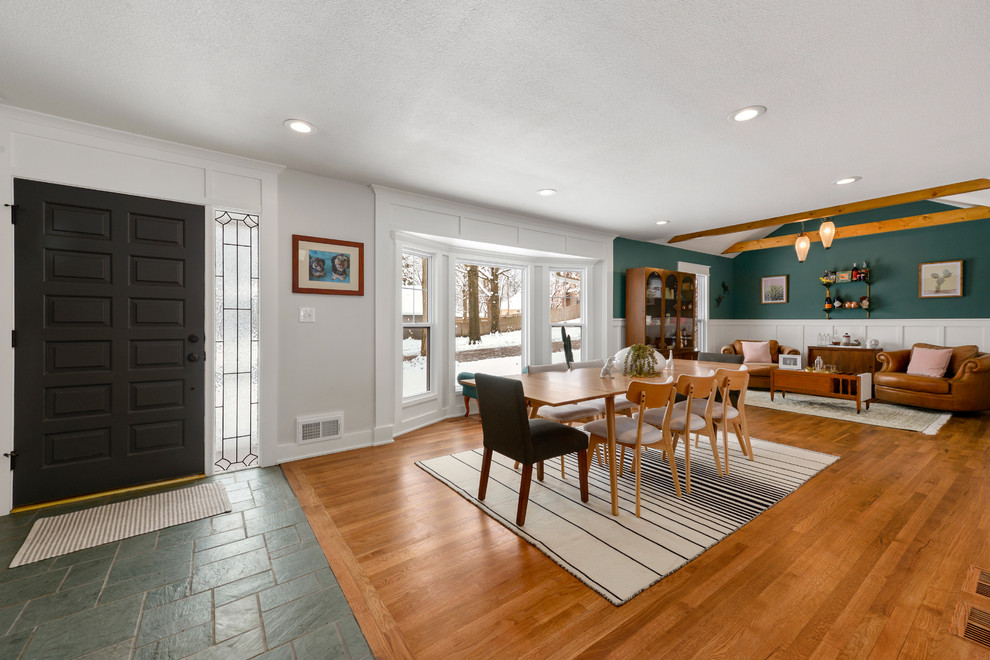 Cette photo montre une salle à manger ouverte sur le salon chic de taille moyenne avec un mur blanc, un sol en bois brun, une cheminée standard et un manteau de cheminée en brique.