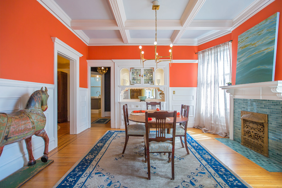 Idee per una sala da pranzo classica chiusa con pareti arancioni, pavimento in legno massello medio, camino classico e cornice del camino piastrellata