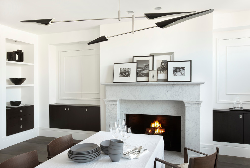 Immagine di una sala da pranzo design con pareti bianche, parquet scuro e camino classico