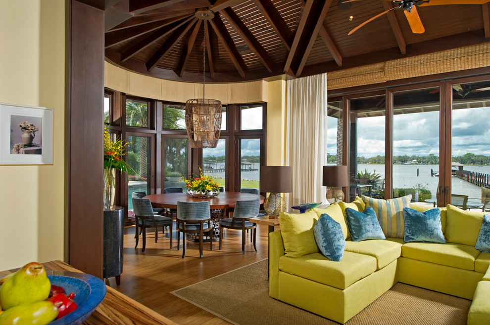 Immagine di una grande sala da pranzo aperta verso il soggiorno tropicale con pareti gialle, pavimento in legno massello medio e nessun camino