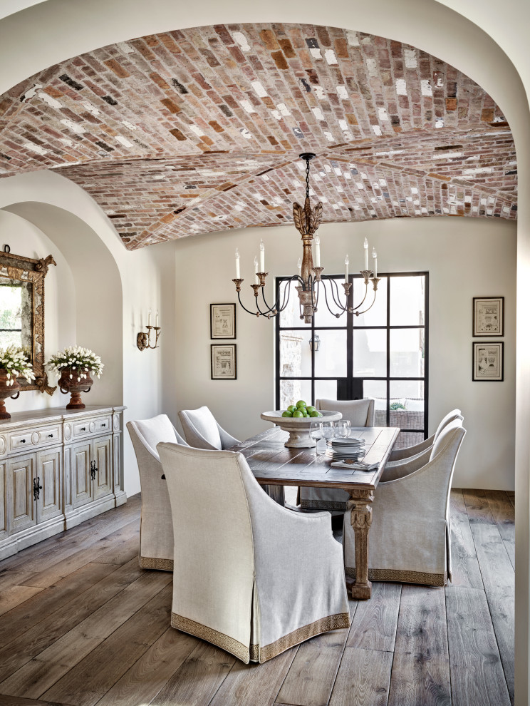 Cette image montre une salle à manger méditerranéenne fermée avec un mur blanc, un sol en bois brun, aucune cheminée, un sol marron et un plafond voûté.