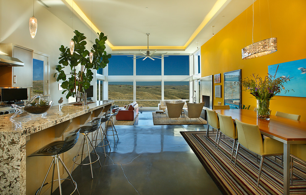 Cette image montre une salle à manger design de taille moyenne avec un mur jaune, sol en béton ciré, une cheminée standard, un manteau de cheminée en métal et un sol gris.