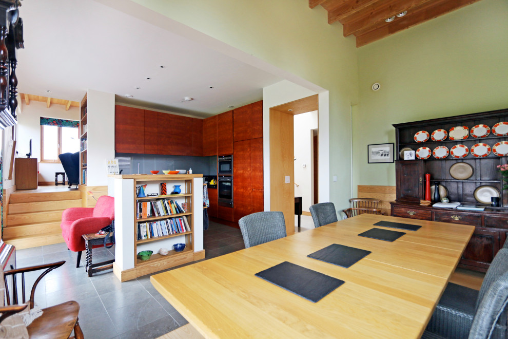 На фото: большая кухня-столовая в современном стиле с зелеными стенами, полом из известняка, серым полом, балками на потолке и панелями на части стены