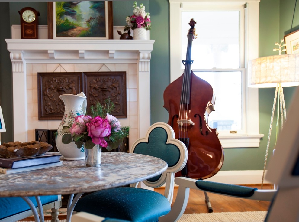 Cette photo montre une salle à manger ouverte sur le salon tendance de taille moyenne avec un mur vert, un sol en bois brun, une cheminée standard et un manteau de cheminée en béton.