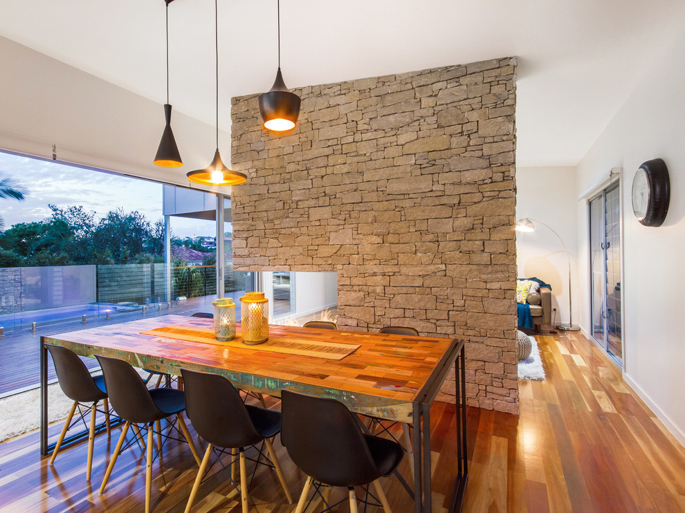 Imagen de comedor de cocina actual de tamaño medio con paredes blancas, suelo de madera en tonos medios, chimenea de doble cara y marco de chimenea de piedra