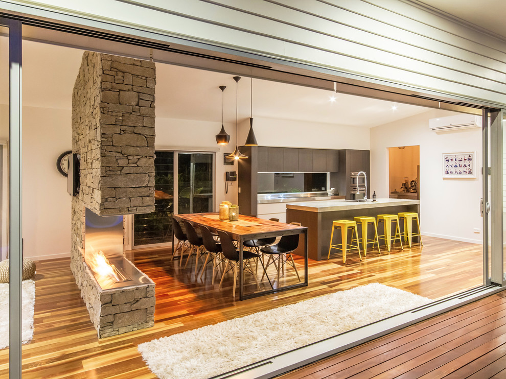 Mittelgroße Moderne Wohnküche mit weißer Wandfarbe, braunem Holzboden, Tunnelkamin und Kaminumrandung aus Stein in Brisbane