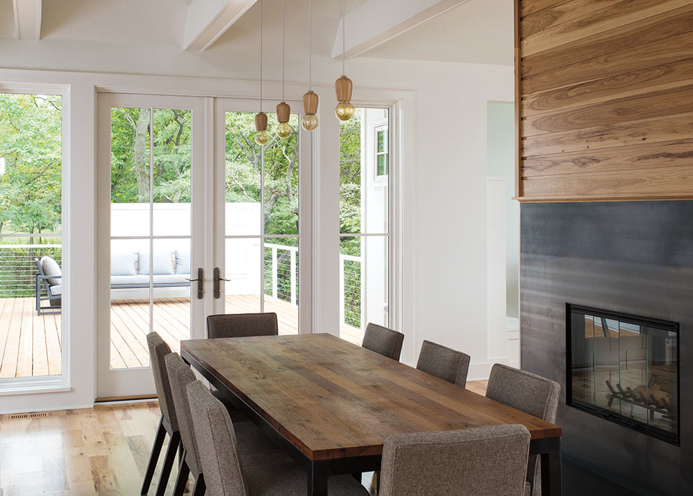 Cette image montre une salle à manger ouverte sur le salon minimaliste de taille moyenne avec un mur blanc, parquet clair, une cheminée double-face, un manteau de cheminée en métal et un sol marron.