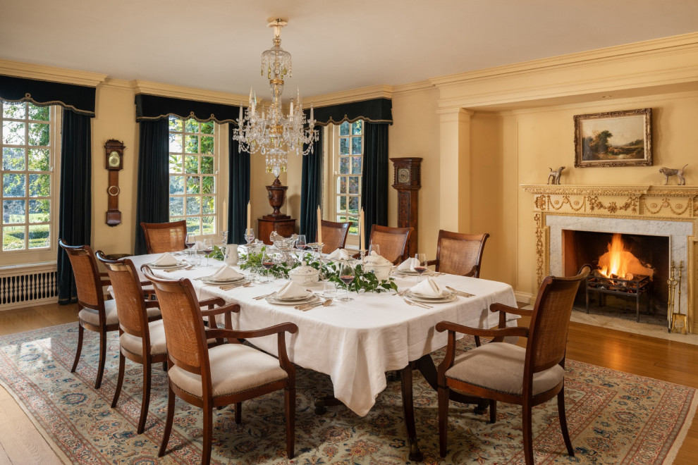 Foto di una grande sala da pranzo aperta verso la cucina classica con pareti gialle, pavimento marrone, camino classico e pavimento in legno massello medio