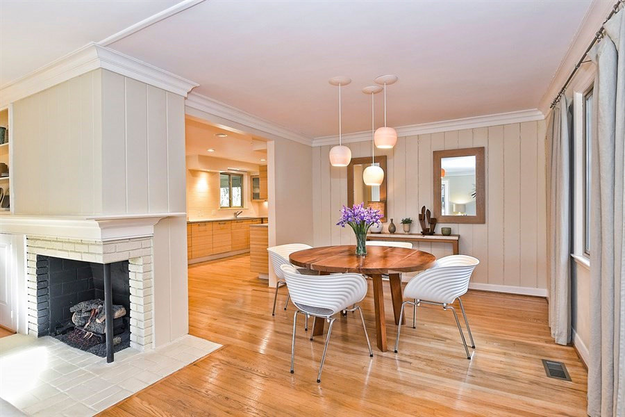 Aménagement d'une salle à manger ouverte sur la cuisine rétro de taille moyenne avec un mur beige, un sol en bois brun, une cheminée d'angle et un manteau de cheminée en brique.