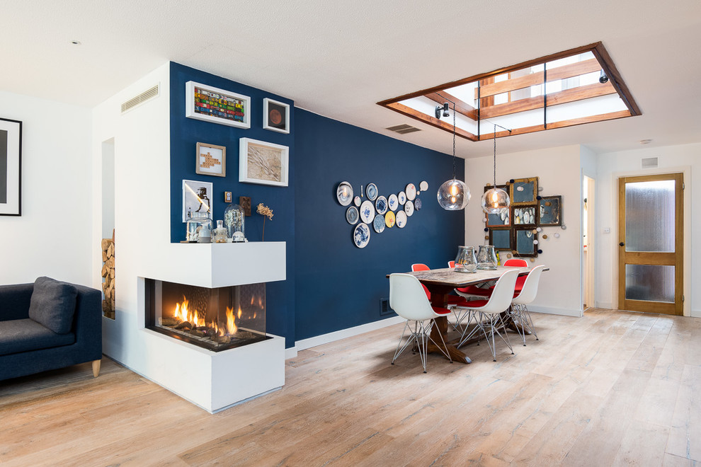 Modelo de comedor contemporáneo de tamaño medio abierto con paredes azules, suelo de madera clara y chimenea de doble cara