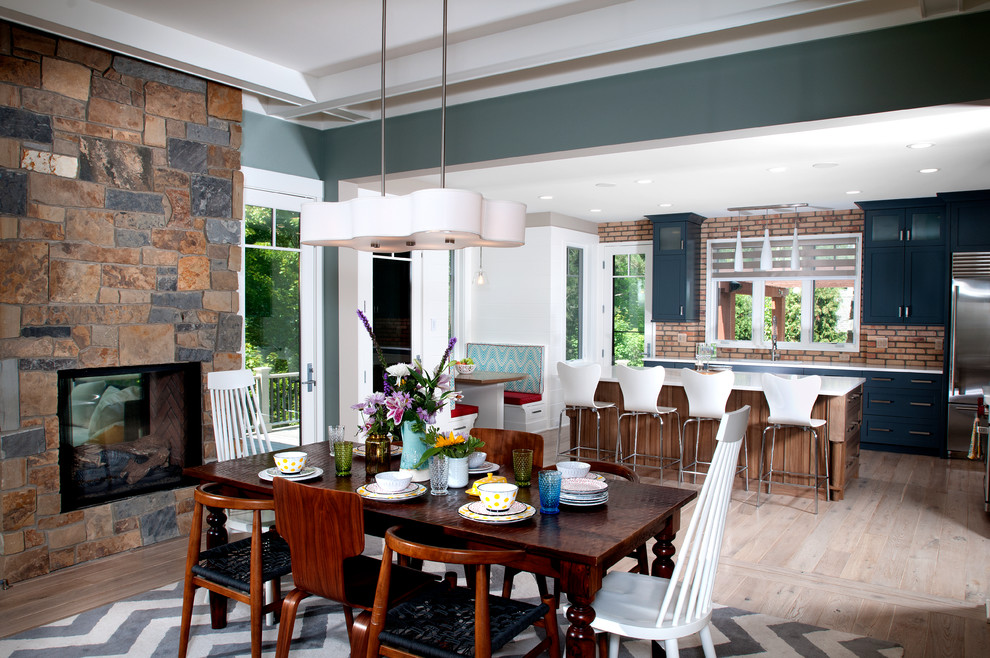 Foto di una sala da pranzo aperta verso il soggiorno chic di medie dimensioni con pareti blu, parquet chiaro, camino bifacciale e cornice del camino in pietra