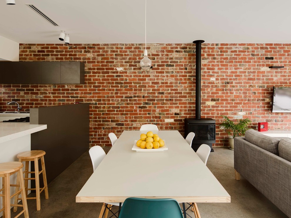 Idee per una sala da pranzo aperta verso il soggiorno industriale con pavimento in cemento, stufa a legna, cornice del camino in metallo e pavimento grigio