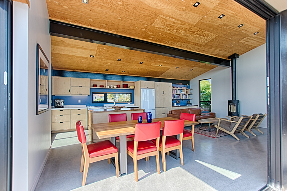 Exemple d'une petite salle à manger tendance avec un mur bleu, sol en béton ciré, un poêle à bois, un manteau de cheminée en métal et un sol gris.