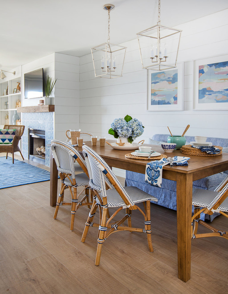 Aménagement d'une salle à manger ouverte sur le salon bord de mer de taille moyenne avec un mur blanc, un sol en bois brun, une cheminée standard et un manteau de cheminée en carrelage.