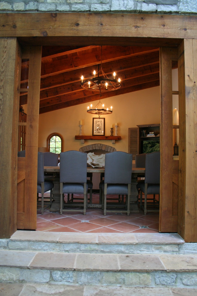 Exemple d'une salle à manger chic avec un mur beige, tomettes au sol, une cheminée standard et un manteau de cheminée en brique.