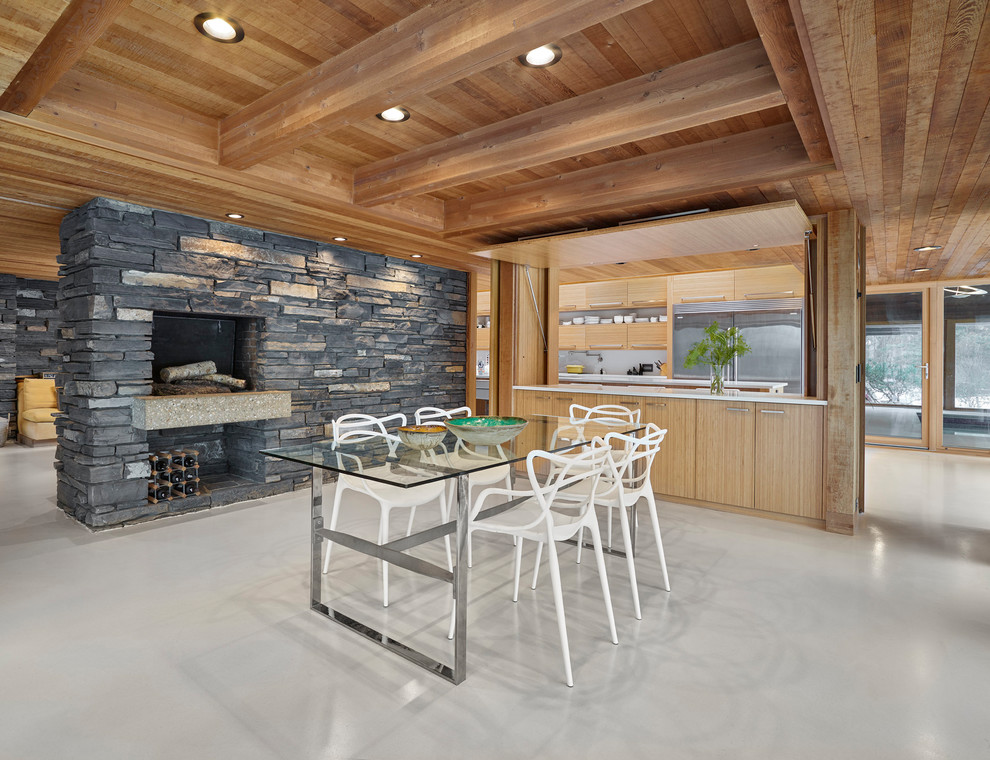 This is an example of a large rustic open plan dining room in Edmonton with a standard fireplace, a stone fireplace surround, white floors, brown walls and concrete flooring.