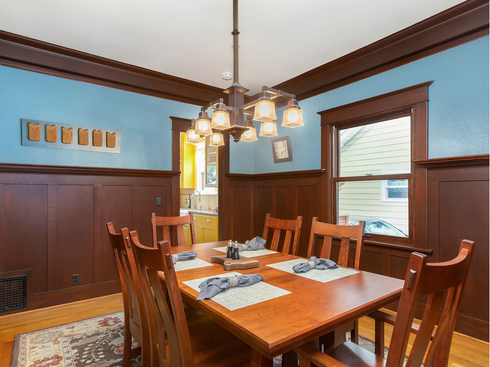 Cette photo montre une grande salle à manger craftsman fermée avec un mur bleu, un sol en bois brun et aucune cheminée.