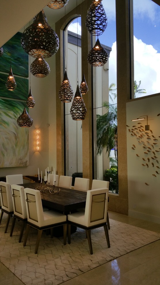 Immagine di una grande sala da pranzo aperta verso il soggiorno tropicale con pareti beige, pavimento in pietra calcarea e nessun camino