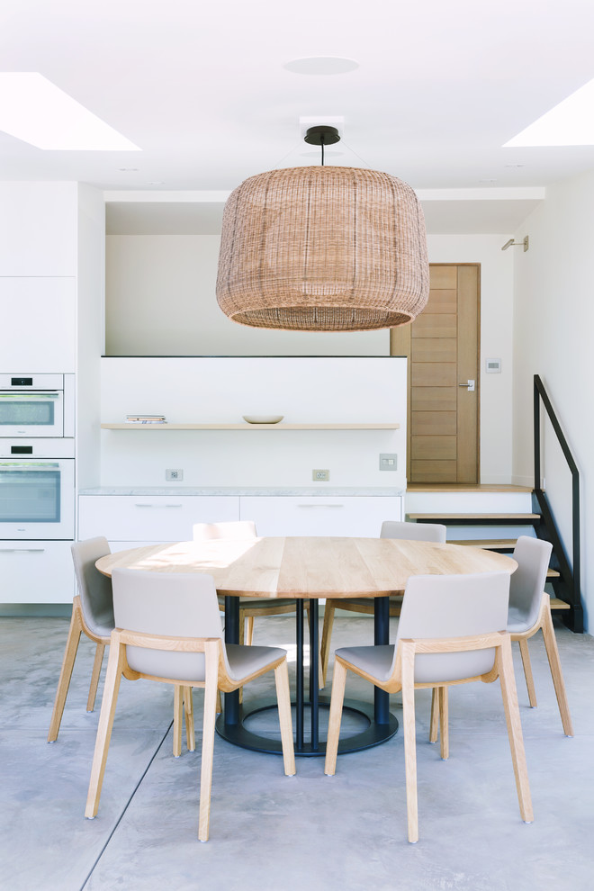 Cette image montre une salle à manger design avec un mur blanc, sol en béton ciré et un sol marron.