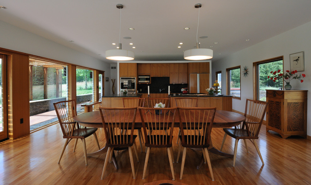 Idée de décoration pour une salle à manger ouverte sur la cuisine minimaliste avec un mur blanc et un sol en bois brun.