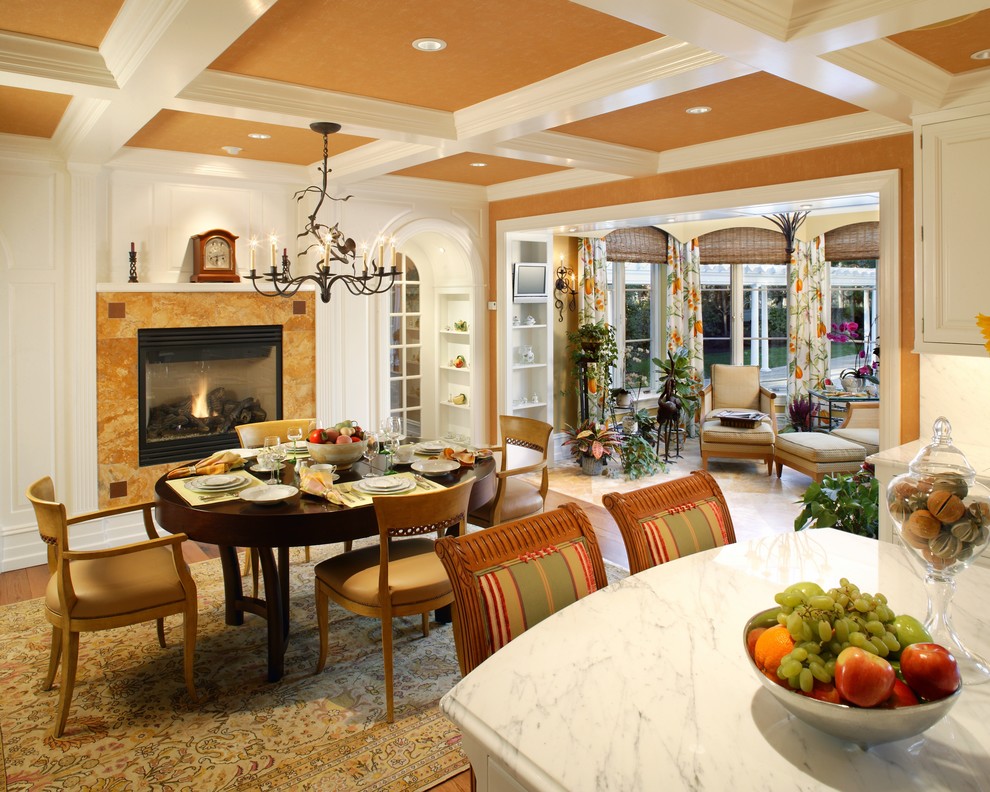 Idée de décoration pour une grande salle à manger tradition avec un mur orange, un sol en bois brun, une cheminée standard et un manteau de cheminée en pierre.