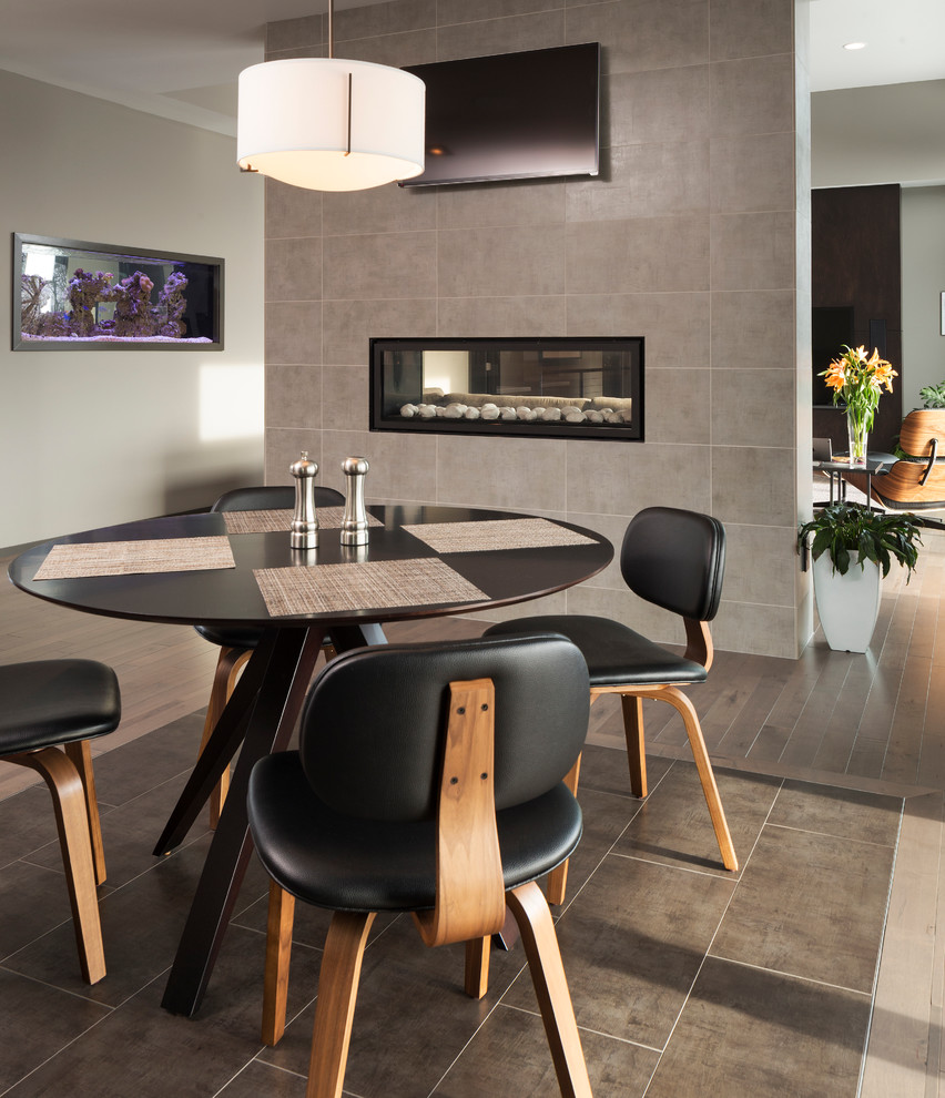 На фото: гостиная-столовая в современном стиле с серыми стенами, двусторонним камином и фасадом камина из плитки
