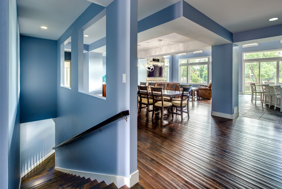 Idée de décoration pour une grande salle à manger ouverte sur la cuisine marine avec un mur bleu, parquet foncé et un manteau de cheminée en pierre.