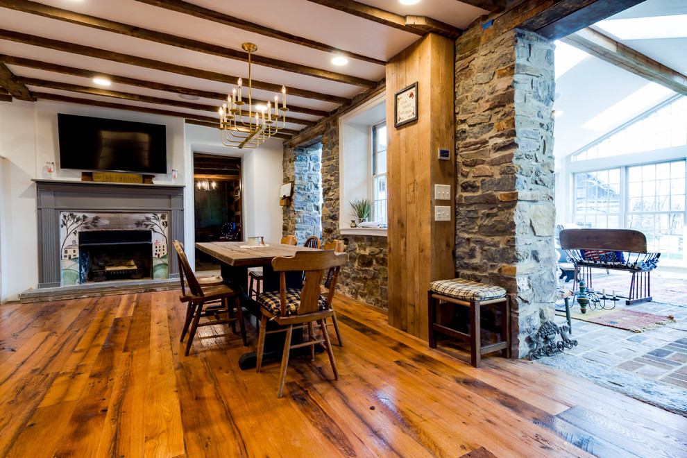 Réalisation d'une grande salle à manger ouverte sur la cuisine champêtre avec un mur beige, un sol en bois brun, une cheminée standard, un manteau de cheminée en pierre et un sol marron.